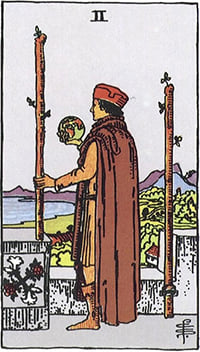 The Two of Wands tarot card: a man on a battlement holding a small globe, looking out to sea