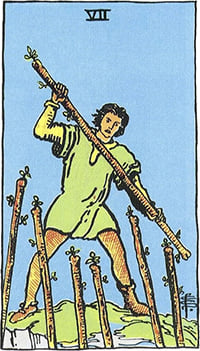 The Seven of Wands tarot card: a man on high ground fending off six staffs raised from below