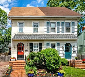 A two-story twin house with a red door and a green door, a brick walk and flower beds