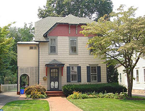 A three-story frame house with a red door, set among trees