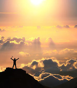 A person on a mountaintop with arms raised above a sea of glowing clouds at sunrise