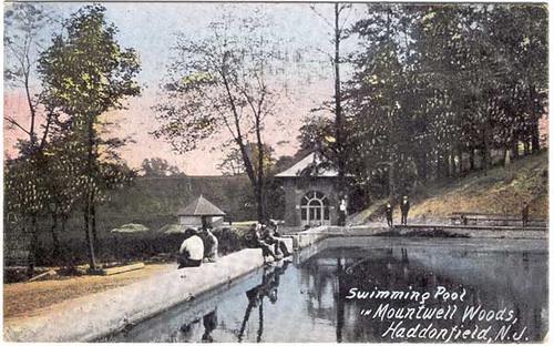 Old hand-tinted postcard of the swimming pool in Mountwell Woods, a bathhouse among the trees