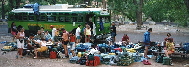 Passengers sorting through piles of bags and bedding spread on the ground beside the bus