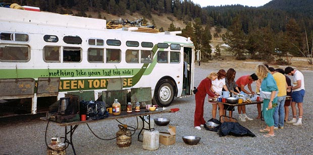 Passengers cooking at tables and camp stoves set up beside the bus