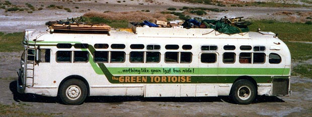 A green and white Green Tortoise bus parked on a dirt lot