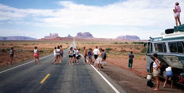 Passengers walking along a road in Monument Valley, the bus parked alongside, buttes in the distance