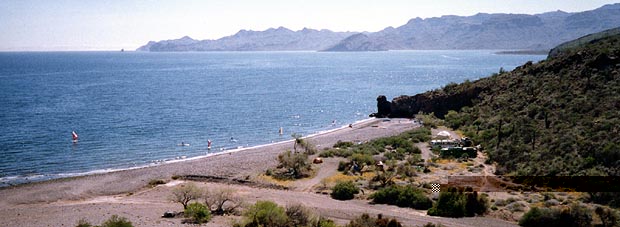 A remote beach curving along a blue bay below dry hills