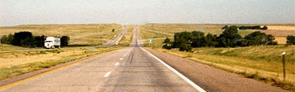 A straight interstate running to the horizon through flat farmland, a truck far ahead